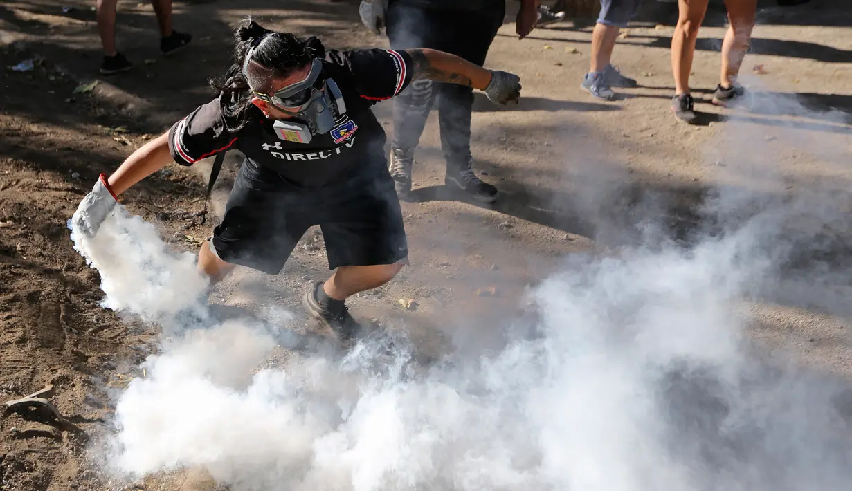 Demonstran mengembalikan tabung gas air mata yang ditembakkan polisi untuk membubarkan protes di Santiago, Chile, Jumat (27/12/2019). Chile terus bergolak menyusul demonstrasi memprotes kenaikan tarif kereta bawah tanah sejak 18 Oktober lalu. (AP Photo/Fernando Llano)