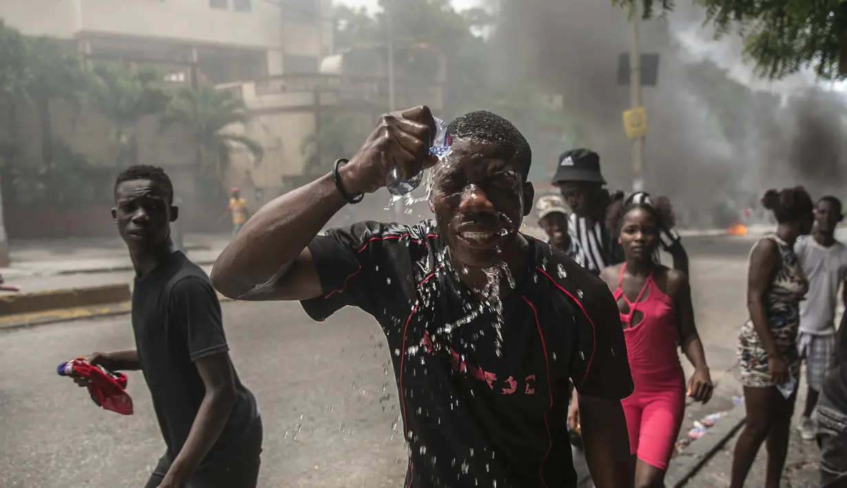 Seorang pengunjuk rasa yang terkena gas air mata polisi memercikkan air ke wajahnya, selama protes menuntut Perdana Menteri Haiti Ariel Henry mundur dan menyerukan kualitas hidup yang lebih baik, di Port-au-Prince, Haiti, Senin (29/8/2022). (AP Photo/Odelyn Joseph)