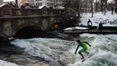 Sejumlah orang dari atas jembatan menyaksikan para pelancar beraksi menaklukkan ombak Sungai Eisbach di Munich, Jerman, 4 Januari 2017. Sungai Eisbach selalu dipadati para peselancar sepanjang tahun, tidak bergantung musim. (Mark RALSTON/AFP)