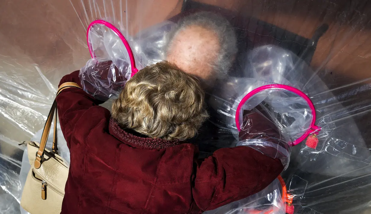 Diane Rossi (Kiri) memeluk suaminya, Arthur Rossi, melalui tenda pelukan di komunitas Crossroads Senior Living di Lakewood, Colorado, Jumat (26/2/2021). Tenda dengan penghalang plastik memungkinkan anggota keluarga terhubung secara fisik satu sama lain. (Michael Ciaglo/Getty Images/AFP)