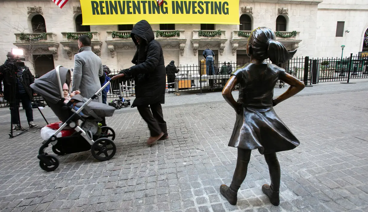 Orang-orang melewati patung "Fearless Girl" setelah diresmikan di lokasi barunya di depan bursa efek New York, Selasa (11/12). Patung yang menginspirasi dengan pesan feminisme itu sebelumnya berada di depan patung 'Charging Bull'. (AP/Mark Lennihan)