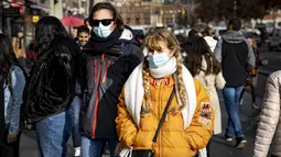 Orang-orang dengan masker melintasi jalan di pusat kota Amsterdam, Belanda, Rabu (3/11/2021). Dengan aturan terbaru, pemerintah Belanda mewajibkan penggunaan masker di ruang-ruang publik seperti tempat perbelanjaan, perpustakaan, salon, stasiun kereta, hingga rumah sakit. (Ramon van Flymen/ANP/AFP)