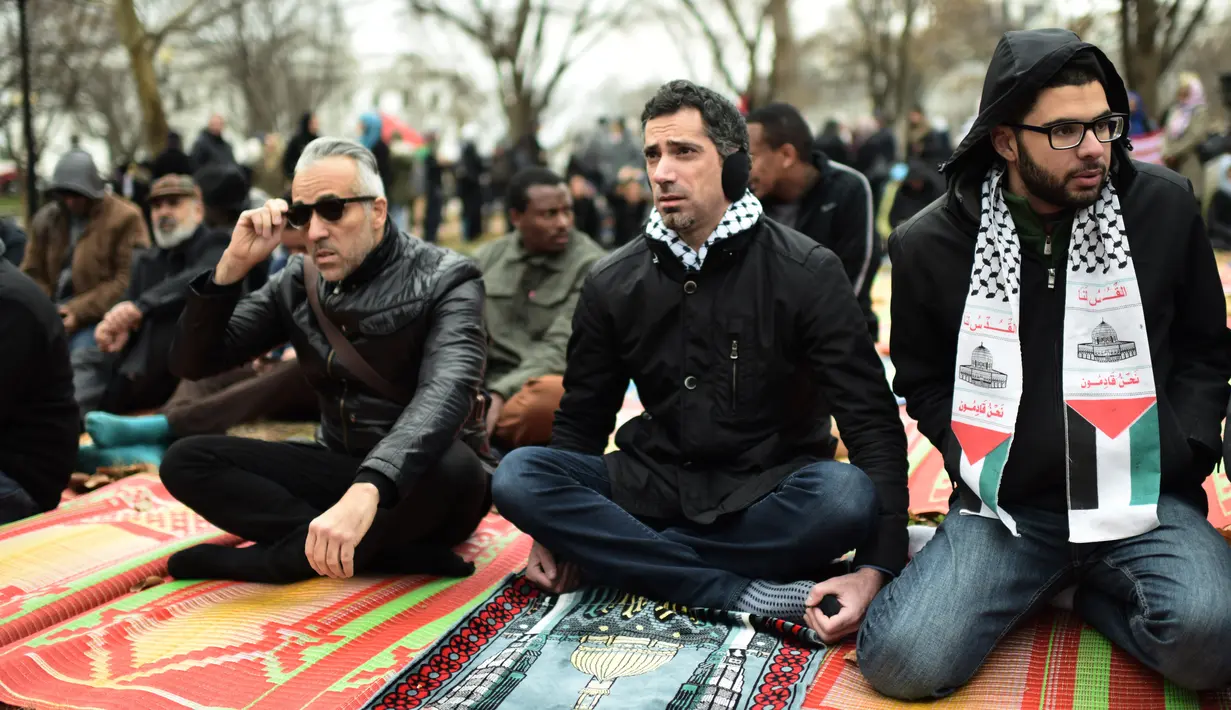 Warga Muslim mendengarkan ceramah saat menggelar Salat Jumat berjamaah di depan Gedung Putih, Jumat (8/12). Para warga muslim ini menggelar sajadah mereka di sebuah taman yang ada di depan kediaman resmi Presiden AS Donald Trump. (Eric BARADAT / AFP)