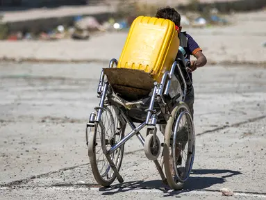 Dalam foto yang diambil pada 8 Juni 2023 ini, seorang anak laki-laki mendorong kursi roda berisi jerigen untuk diisi dari truk tangki air di pinggiran kota ketiga Yaman, Taez. (AHMAD AL-BASHA / AFP)