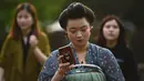 Seorang wanita bermain ponsel saat mengenakan kostum Dinasti Tang di Danau Barat di Hangzhou di provinsi Zhejiang timur China (31/3). Bahan pakaian Dinasti Tang terbuat dari sutra dan terkenal karena kelembutan dan ringan.  (AFP Photo/China Out)