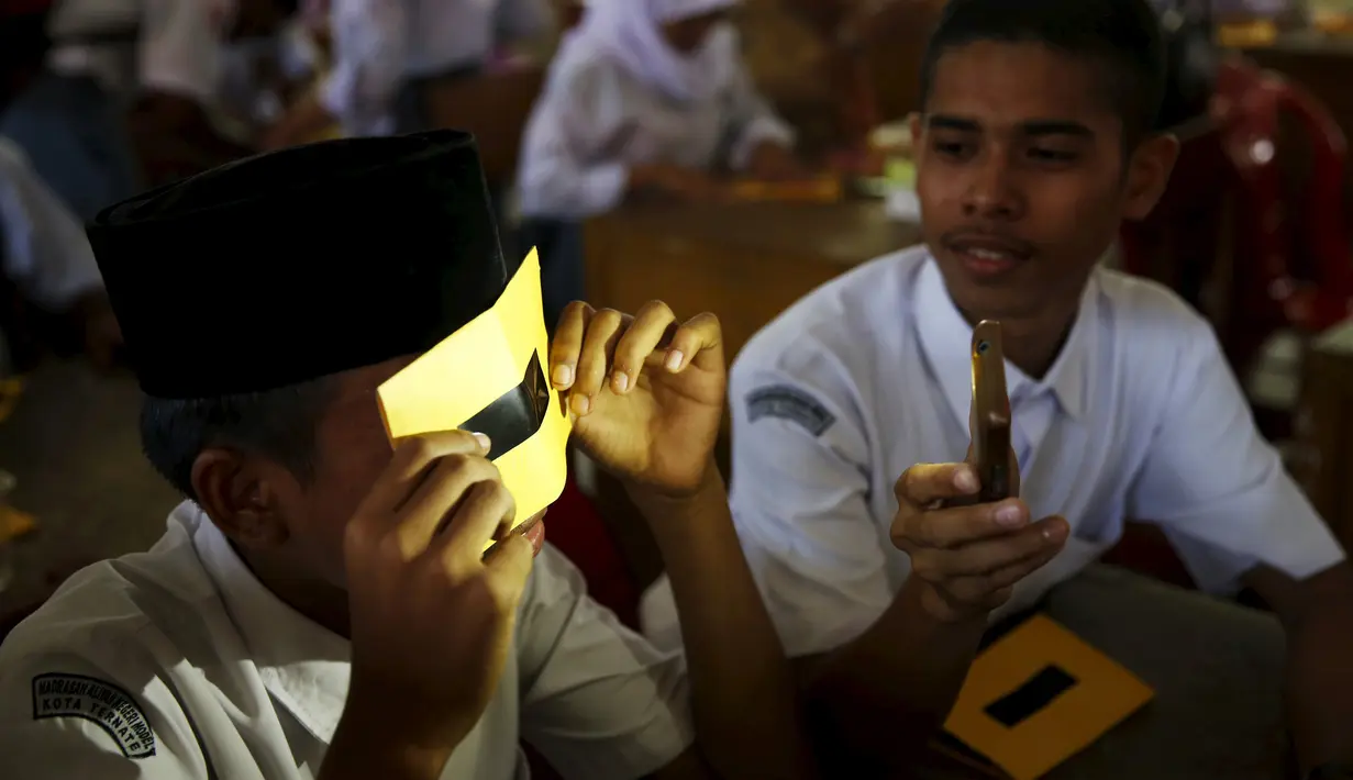 Pelajar menjajal kacamata filter buatan sendiri dengan cahaya senter ponsel dalam workshop di sebuah sekolah di Ternate, (7/3). Kacamata ini akan digunakan untuk mengamati Gerhana Matahari Total. (REUTERS/Beawiharta)