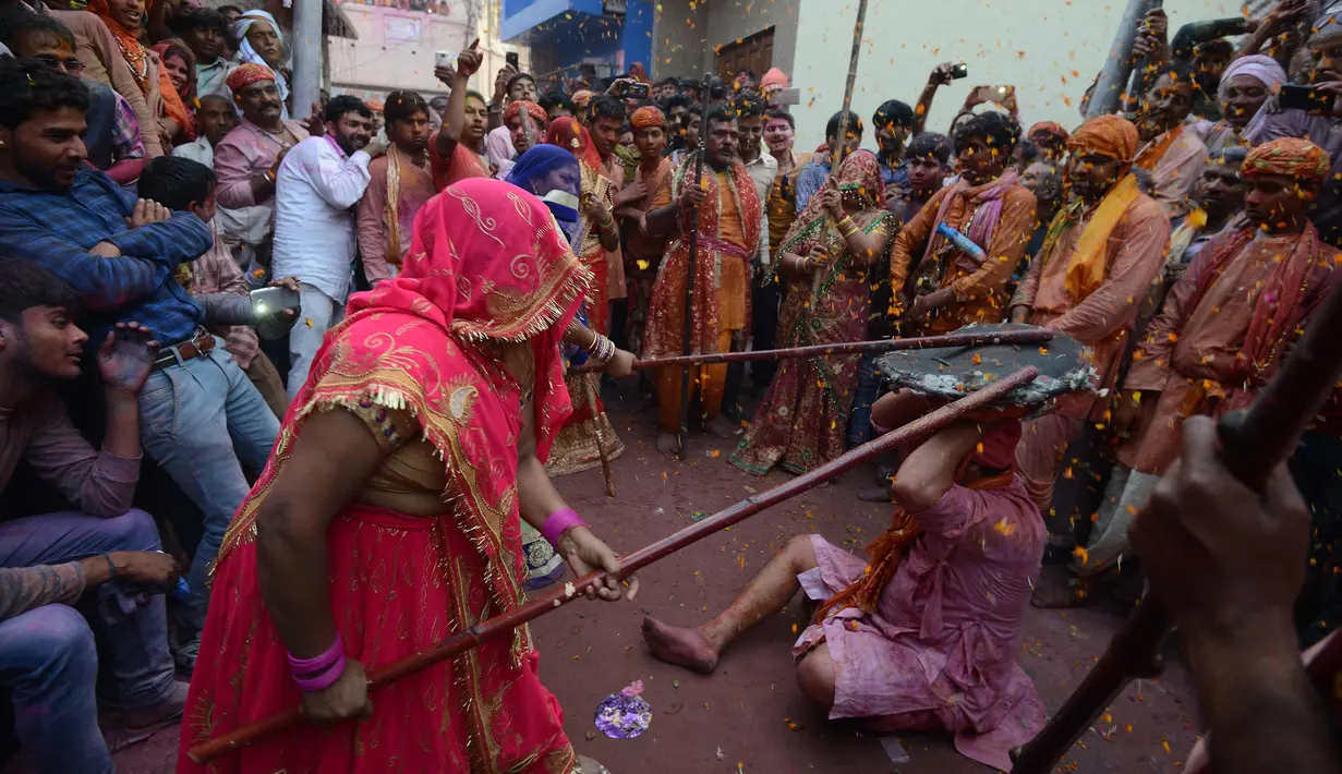 Pria saat dipukuli para wanita dengan tongkat (lathi) selama perayaan Lathmar Holi di Barsana di Mathura, India, (24/2). Lathmar Holi adalah perayaan lokal festival Hindu Holi, biasanya beberapa hari sebelum festival Holi. (AFP Photo/Dominique Faget)