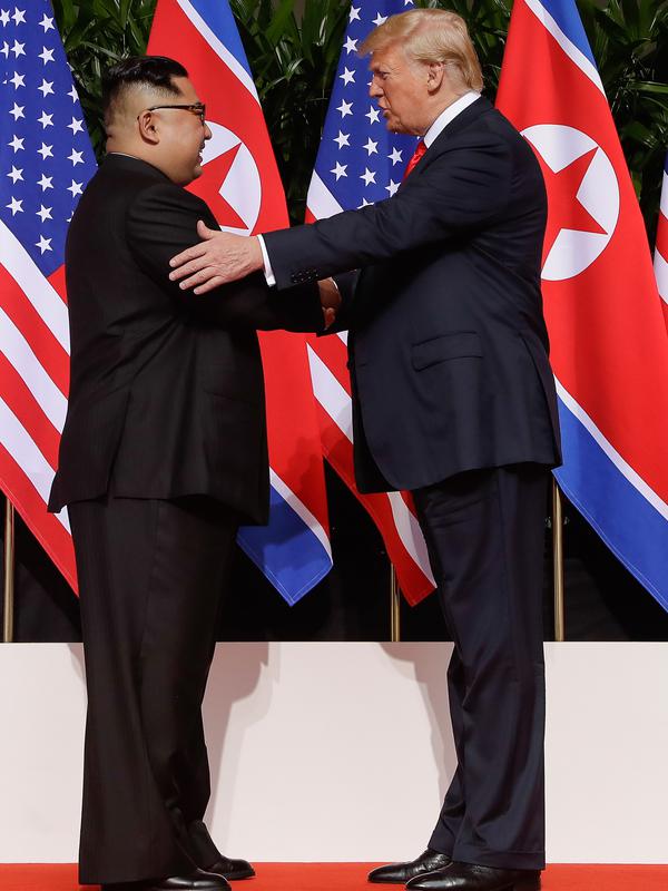 Presiden AS Donald Trump  berjabat tangan dengan Pemimpin Korea Utara, Kim Jong-un dalam pertemuan bersejarah di resor Capella, Pulau Sentosa, Selasa (12/6). Kim dan Trump hadir di depan jurnalis dengan latar belakang bendera Korut dan AS. (AP/Evan Vucci)