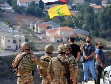 Tentara Lebanon berdiri di sebuah bukit yang menghadap ke Kota Metula di Israel ketika seorang pria mengibarkan bendera Palestina dan Hizbullah di sisi perbatasan Lebanon-Israel di desa selatan Kfar Kila, Lebanon, Senin (9/10/2023). Pasukan Israel menembak dan membunuh beberapa pria bersenjata yang menyeberang ke negara itu dari Lebanon, kata Pasukan Pertahanan Israel tanpa menyebutkan jumlah orang yang terbunuh atau dugaan afiliasi mereka. (AP Photo/Mohammed Zaatari)