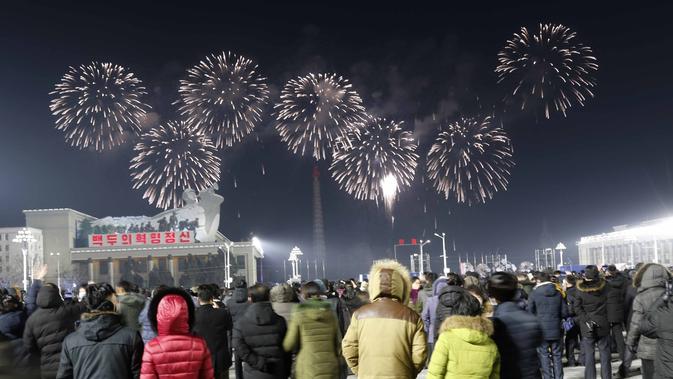 Pertunjukan kembang api menghiasi langit malam untuk merayakan Tahun Baru, saat kerumunan orang melihatnya, di Alun-alun Kim Il Sung di Pyongyang, Korea Utara, Jumat pagi, 1 Januari 2021. (AP Photo/Jon Chol Jin)