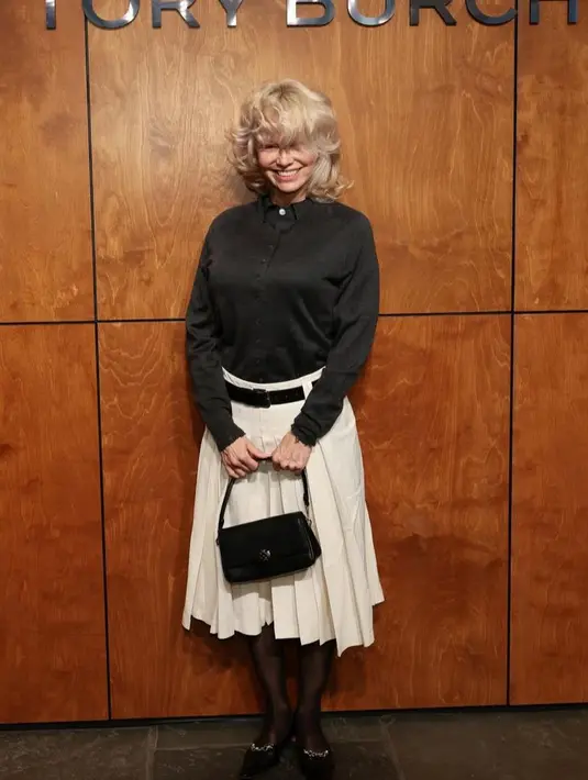 Pamela Anderson tampil chic dengan silk knit cardigan dan polo yang dipadukan rok paper cotton serta mantel wol double-breasted. Tas Charlie berukuran kecil dan barbed wire pumps menambah kesan polished yang effortless. [dok/toryburch].