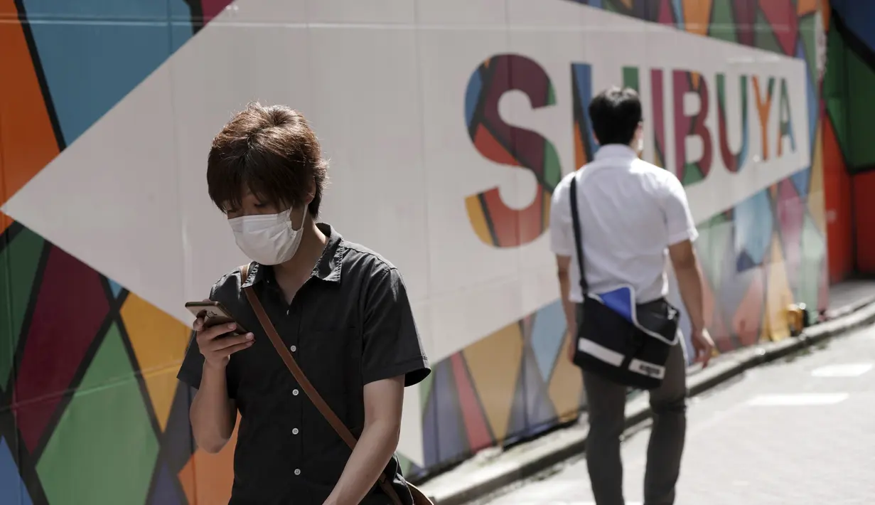 Seorang pria yang mengenakan masker berjalan di jalan belakang di distrik Shibuya, Tokyo, Kamis (30/9/2021). Jepang akan mencabut keadaan darurat COVID-19 di semua wilayah pada akhir September. (AP Photo/Eugene Hoshiko)