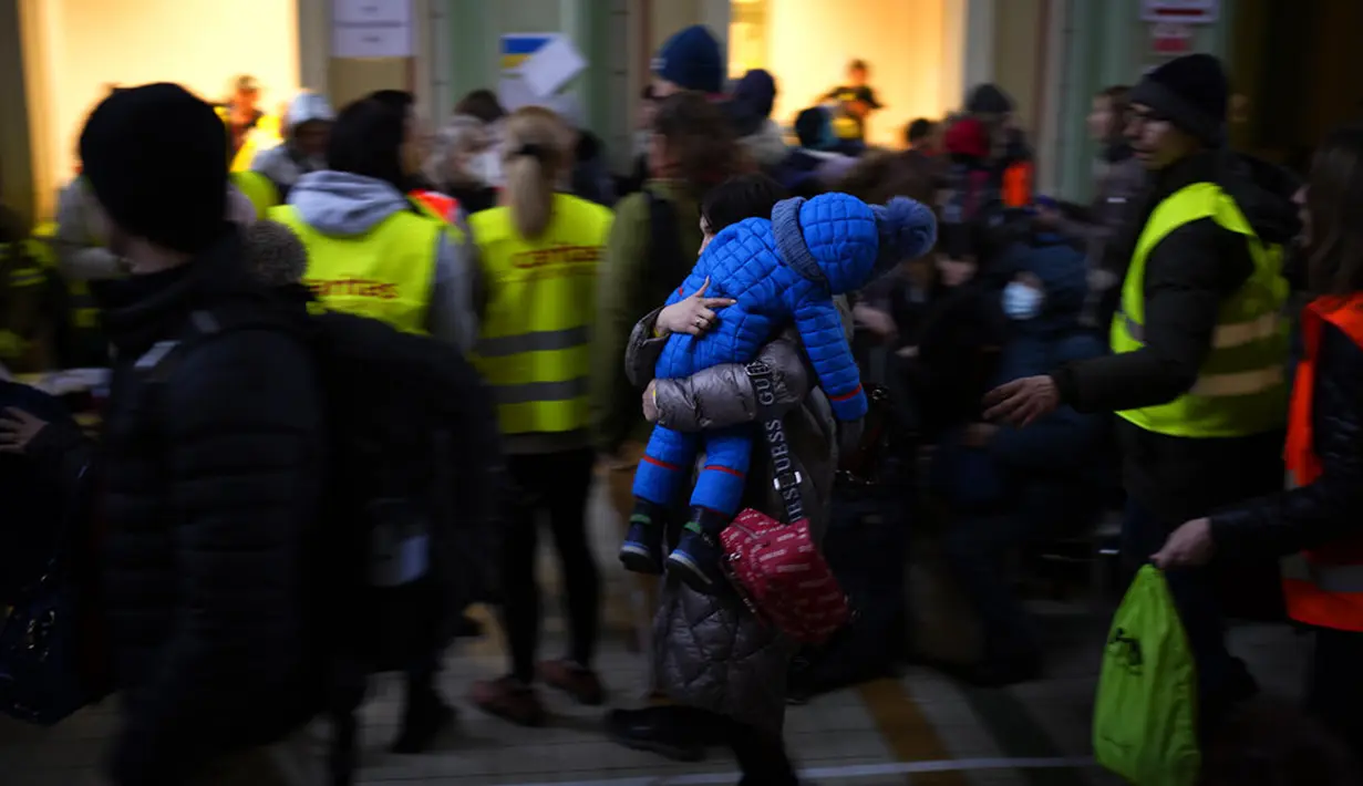 Seorang wanita menggendong seorang anak dalam setelan musim dingin setelah melarikan diri dari Ukraina dan tiba di stasiun kereta api di Przemysl, Polandia, 8 Maret 2022. PBB mengatakan, serangan gencar Rusia telah memaksa lebih dari 2 juta orang meninggalkan Ukraina. (AP Photo/Daniel Cole)