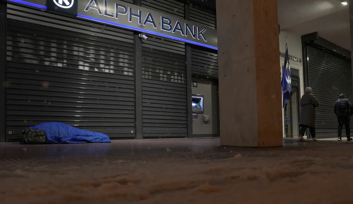 Tunawisma tidur di luar bank saat hujan salju di Athena, Yunani, Senin (24/1/2022). Hujan salju lebat mengganggu lalu lintas udara di Athena dan kota tetangga terbesar Turki, Istanbul, sementara beberapa pulau Aegea dan sebagian besar wilayah Turki diselimuti salju. (AP Photo/Thanassis Stavrakis)