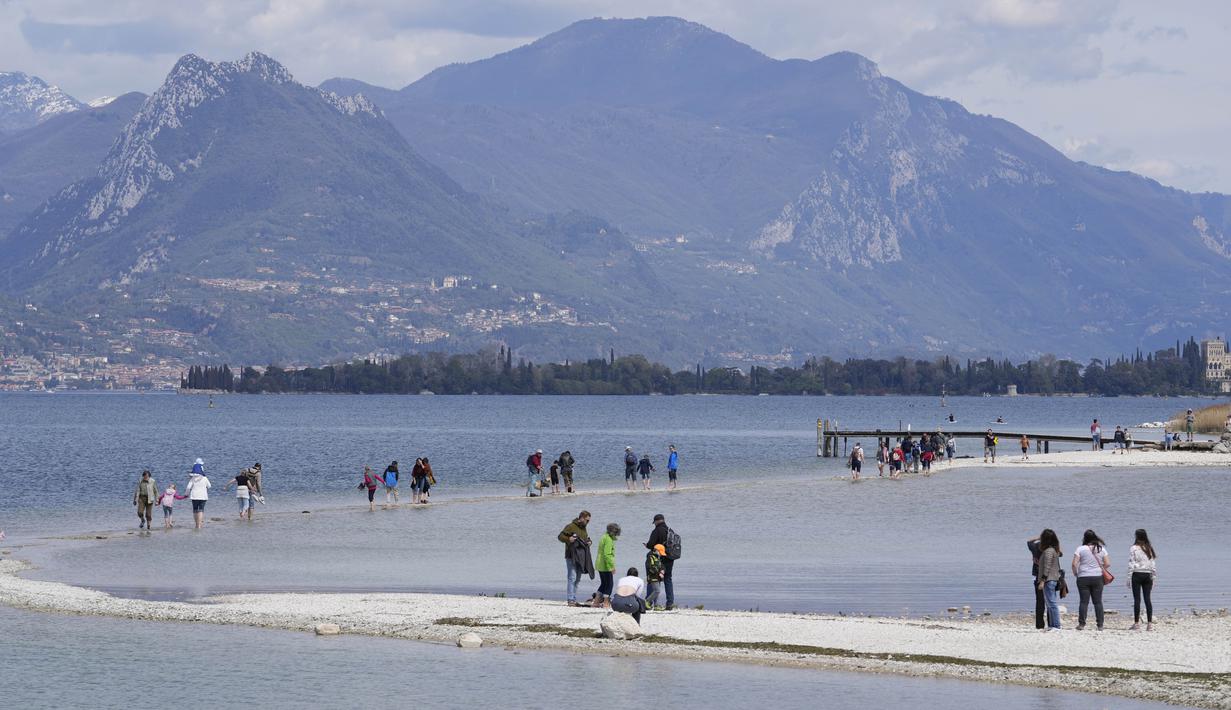 Wisatawan menyeberangi bentangan antara daratan dan pulau San Biagio di Manerba, di Danau Garda, Italia, Jumat, 14 April 2023. (AP Photo/Luca Bruno)