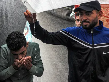 Salah satu pengungsi menggunakan tangan untuk meminum air hujan yang menetes dari atap tenda pengungsian yang dikelola oleh Badan Bantuan dan Pekerjaan Perserikatan Bangsa-Bangsa (PBB) untuk Pengungsi Palestina di Rafah, Jalur Gaza Selatan pada 14 November 2023. (SAID KHATIB/AFP)
