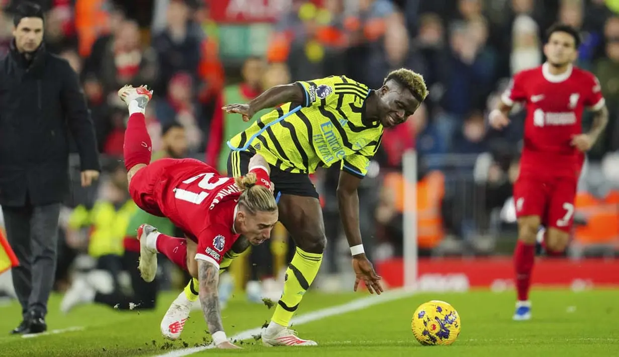 Pemain Liverpool, Kostas Tsimikas, berebut bola dengan pemain Arsenal, Bukayo Saka pada laga pekan ke-18 Premier League 2023/2024 di Stadion Anfield, Minggu (24/12/2023). pemain asal Yunani itu mengalami cedera tulang selangka yang parah. (AP Photo/Jon Super)