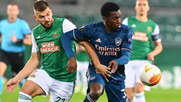 Penyerang Arsenal, Edward Nketiah, berebut bola dengan bek Rapid Vienna, Filip Stojkovic, pada laga Grup B Liga Europa 2020/2021 di Allianz Stadion, Kamis (22/10/2020) malam WIB. Arsenal menang 2-1 atas Rapid Vienna. (AFP/Joe Klamar)