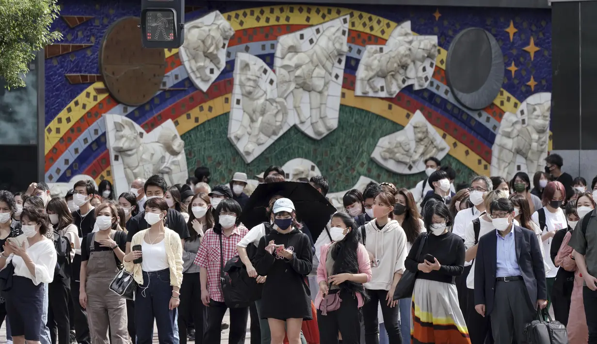 Orang-orang yang memakai masker menunggu untuk berjalan di sepanjang penyeberangan pejalan kaki di distrik Shibuya, Tokyo, Kamis (30/9/2021). Jepang akan mencabut keadaan darurat COVID-19 di semua wilayah pada akhir September. (AP Photo/Eugene Hoshiko)