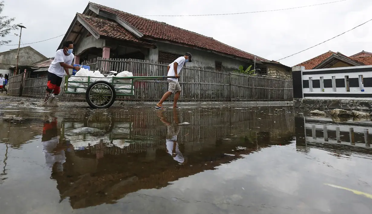 Jurnalis membawa gerobak berisi bantuan sembako di Pulau Panjang, Serang, Banten, Sabtu (30/1/2021). Perwakilan wartawan yang tergabung dalam Jurnalis Peduli menyalurkan bantuan sembako dan uang tunai bagi warga terdampak Covid-19. (Liputan6.com/Pool/JP)