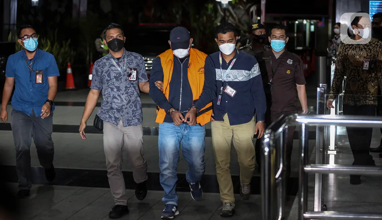 Penyidik Komisi Pemberantasan Korupsi (KPK) menggiring buronan Izil Azhar alias Ayah Merin saat tiba di Gedung KPK, Jakarta, Rabu (25/1/2023).Izil Azhar yang mengenakan jaket berwarna biru dengan dibalut rompi oranye khas tahanan lembaga antirasuah hanya tertunduk tanpa memberikan keterangan apa pun kepada awak media. (Liputan6.com/Johan Tallo)