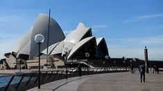 Orang-orang berjalan melalui halaman depan Gedung Opera Sydney yang sepi saat lockdown minggu kedua untuk meredam gejolak varian Delta Covid-19, Selasa (6/7/2021). PM Gladys Berejiklian mengatakan pihaknya akan menentukan nasib lockdown yang sedang diberlakukan di Sydney. (Bianca De Marchi/AFP)
