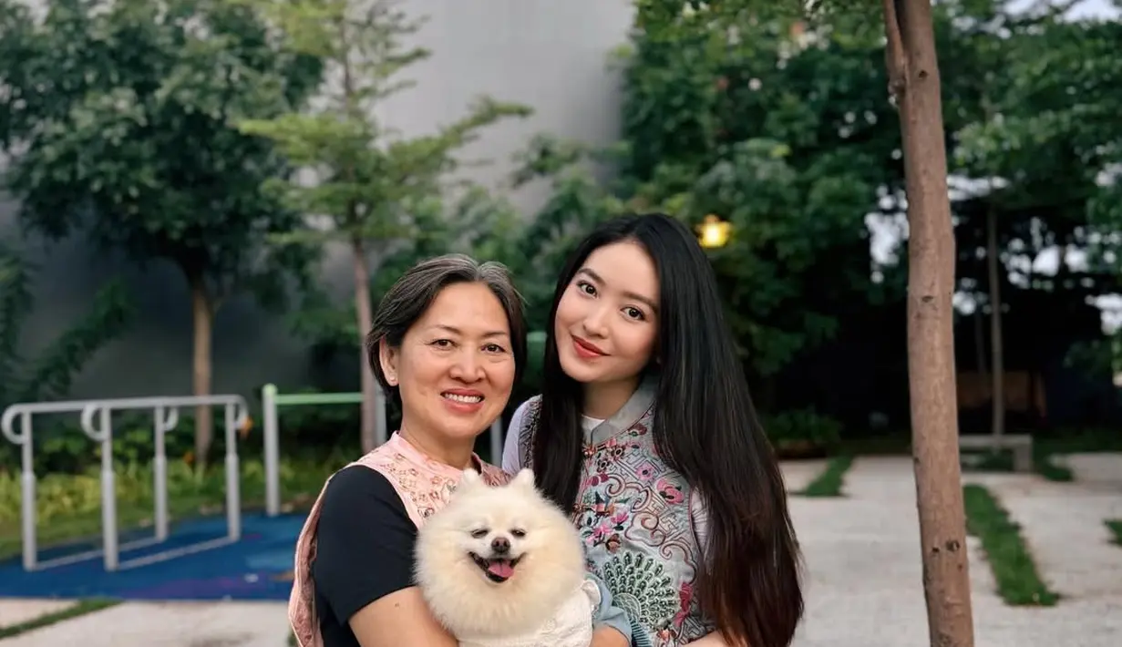Natasha Wilona rayakan Imlek dengan atasan cheongsam biru keabuan berdetail bordir dan celana putih. Sang ibu justru tampil effortless dengan atasan hitam berbalut vest cheongsam dan rok jeans [@natashawilona12]