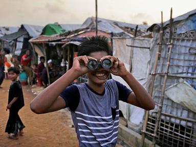 Seorang bocah Rohingya melihat melalui teropong mainan pada perayaan Idul Adha di kamp pengungsi Kutupalong, Bangladesh, Rabu (22/8). Hampir setahun mereka menghuni kamp ini usai kabur menghindari represi militer di Negara Bagian Rakhine. (AP/Altaf Qadri)