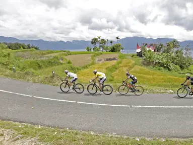 Para pebalap melintasi sawah dan Rumah Gadang pada jalur kelok 44  etape ke-4 Tour de Singkarak 2016 di Kabupaten Agam, Sumatera Barart. (Bola.com/NIcklas anoatubun)