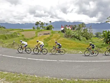 Para pebalap melintasi sawah dan Rumah Gadang pada jalur kelok 44  etape ke-4 Tour de Singkarak 2016 di Kabupaten Agam, Sumatera Barart. (Bola.com/NIcklas anoatubun)