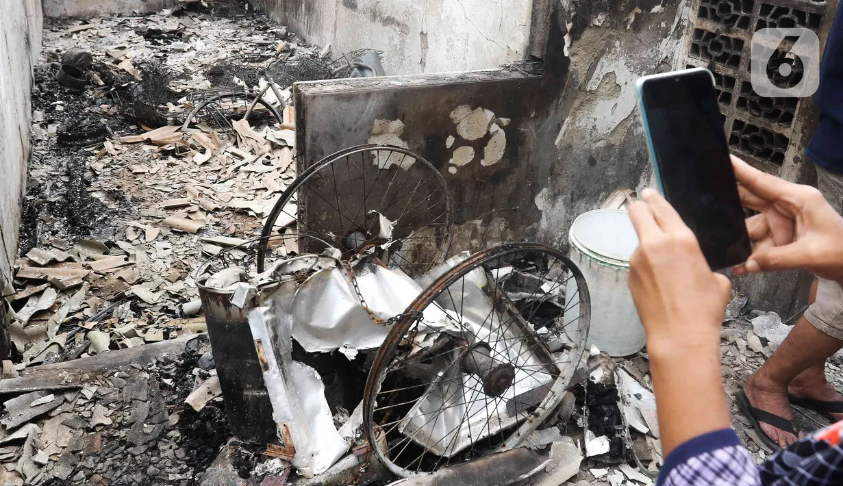 Warga mengambil gambar barang yang hangus terbakar dampak kebakaran Depo Pertamina Plumpang di Jalan Koramil, Rawa Badak, Jakarta, Sabtu (4/3/2023). Polri menyatakan segera mengidentifikasi penyebab kebakaran Depo Pertamina Plumpang, Jakarta Utara pada Jumat, 3 Maret 2023 malam. (Liputan6.com/Herman Zakharia)