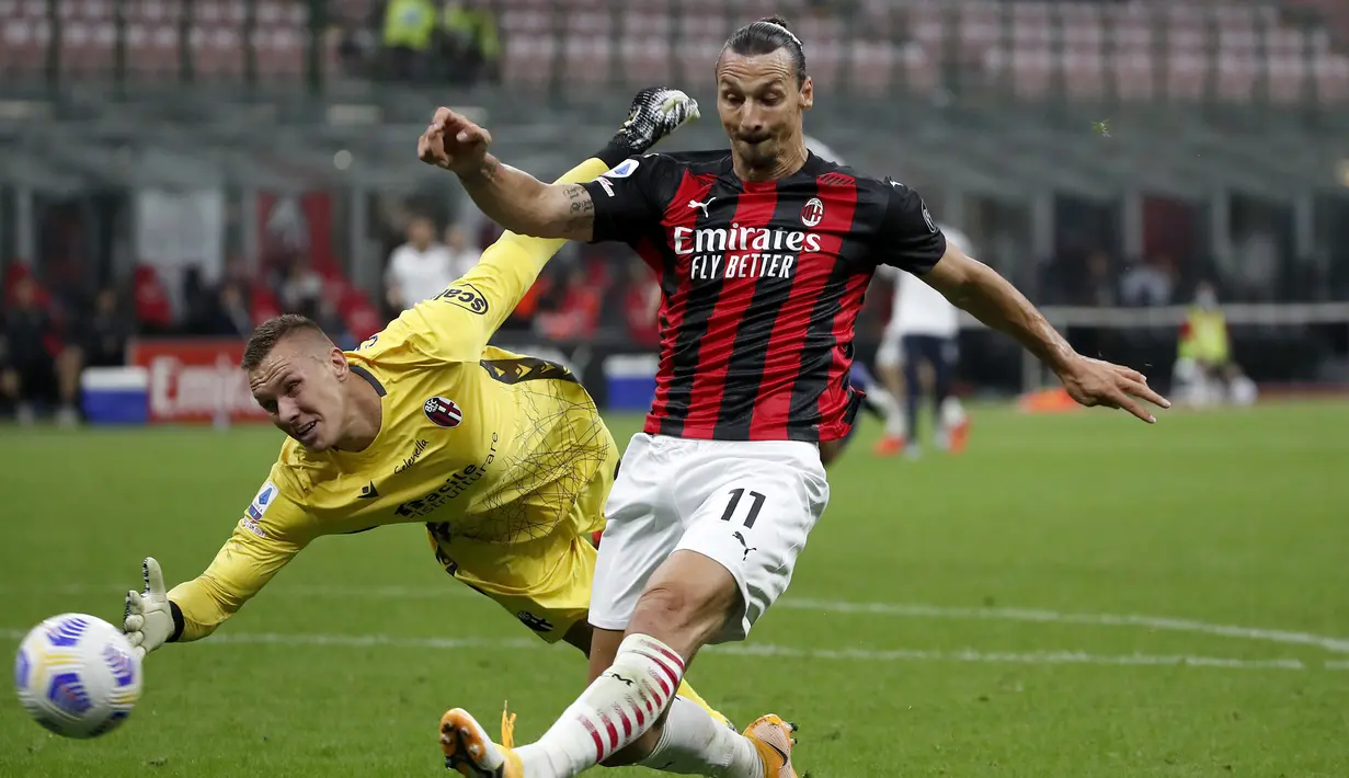 Pemain AC Milan Zlatan Ibrahimovic (kanan) menendang bola saat penjaga gawang Bologna Lukasz Skorupski mencoba menghentikannya pada pertandingan Serie A di Stadion San Siro, Milan, Italia, Senin (21/9/2020). AC Milan menaklukkan Bologna 2-0. (AP Photo/Antonio Calanni)