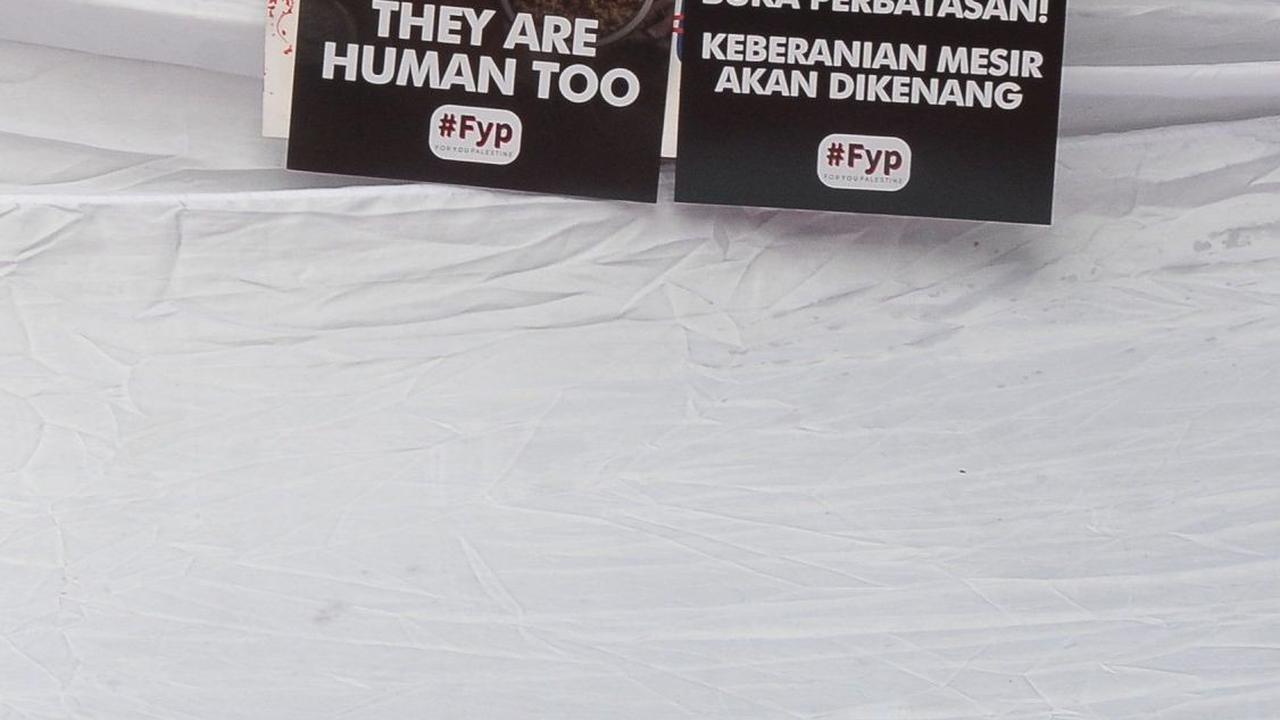 Salah seorang demonstran menunjukkan poster bergambar warga Gaza yang berdesakan sedang mengantre makanan dan antrean truk bantuan yang tertahan di perbatasan Mesir. Foto merdeka.com / Imam Buhori