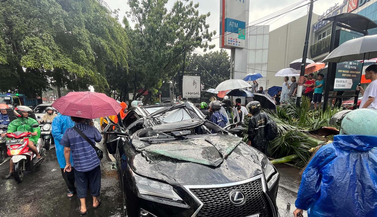 Sebuah mobil mewah bermerek Lexus tertimpa pohon tumbang di Jalan Metro Pondok Indah, Jakarta, Minggu (26/10/2025). (merdeka.com/Arie Basuki)