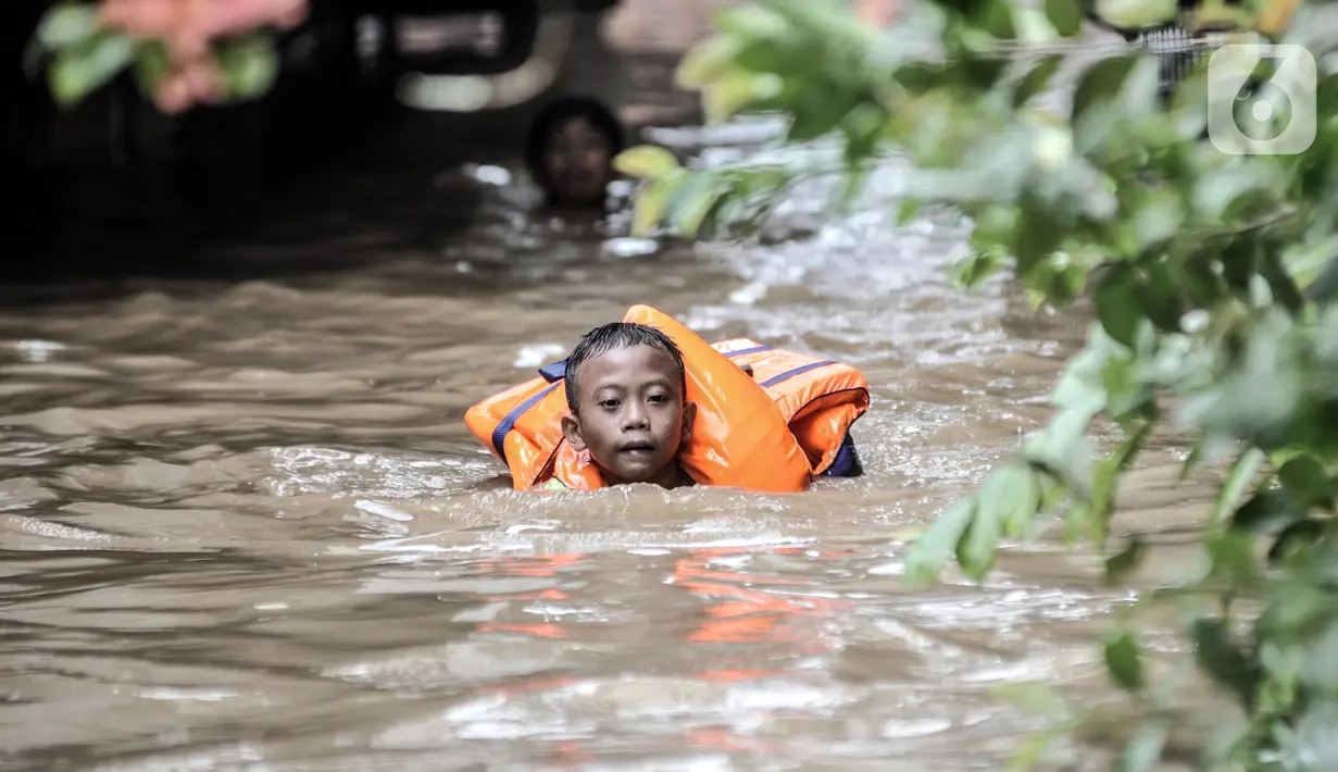 Seorang anak mengenakan pelampung saat menyusuri banjir yang merendam permukiman di Kebon Pala, Jakarta, Senin (8/2/2021). Banjir di Kebon Pala terus meninggi pada dini hari tadi hingga mencapai ketinggian 2,5 meter.  (merdeka.com/Iqbal S. Nugroho)
