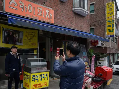 Seorang pria berpose di depan foto sutradara film Bong Joon-ho di restoran pizza bernama 'Sky Pizza' di Seoul, 13 Februari 2020. Lokasi syuting Parasite di Korea Selatan semakin ramai dikunjungi turis setelah film tersebut berhasil memboyong dan mendominasi di penghargaan Oscar 2020. (Ed JONES/AFP)