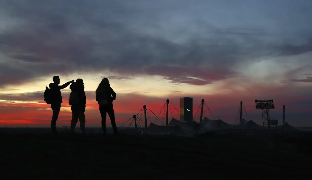 Orang-orang menyaksikan matahari terbenam di taman Olimpiade, Jerman (22/11/2020). Taman Olimpiade ini dibangun untuk Olimpiade Musim Panas 1972. (AP Photo/Matthias Schrader)