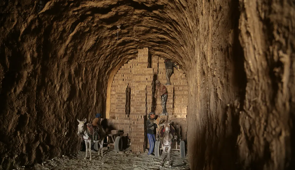 Pekerja memuat batu bata ke gerobak keledai di sebuah pabrik batu bata di pinggiran tenggara Baghdad Nahrawan, Irak, Kamis (24/5/2021).  Para pekerja bekerja 12 jam sehari dengan upah sekitar USD$ 15. (AP Photo/Hadi Mizban)