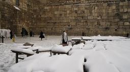 Seorang pria Yahudi ultra-Ortodoks berdiri di atas salju sambil berdoa di Tembok Barat, situs paling suci di mana orang Yahudi dapat berdoa di kota tua Yerusalem, Kamis (27/1/2022). Hujan salju yang jarang melanda sebagian wilayah Israel dan Tepi Barat, menutup sekolah dan bisnis. (AP Photo/Mahmoud