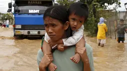 Seorang Perempuan menggendong anaknya melewati jalanan banjir di Nueva Ecija,  Filipina, Senin (19/10/2015). Topan yang memiliki kecepatan angin 175 kilometer per jam ini telah menciptakan gelombang ombak setinggi empat meter. (REUTERS/Erik De Castro)