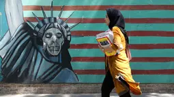 Seorang wanita berjalan melewati lukisan mural yang menggambarkan Patung Liberty di sepanjang dinding bekas Kedutaan Amerika Serikat (AS) di Ibu Kota Teheran, Iran, Sabtu (22/6/2019). (ATTA KENARE/AFP)