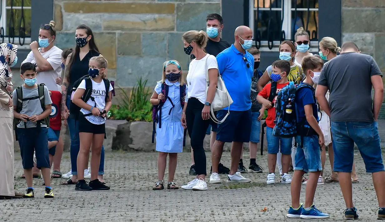 Para orang tua bersama anak mereka menunggu di halaman sekolah untuk memulai hari pertama mereka di Gelsenkirchen, Jerman, Rabu (12/8/2020). Para siswa di negara bagian Jerman, North Rhine-Westphalia, harus mengenakan masker setiap waktu ketika mereka kembali ke sekolah. (AP Photo/Martin Meissner)