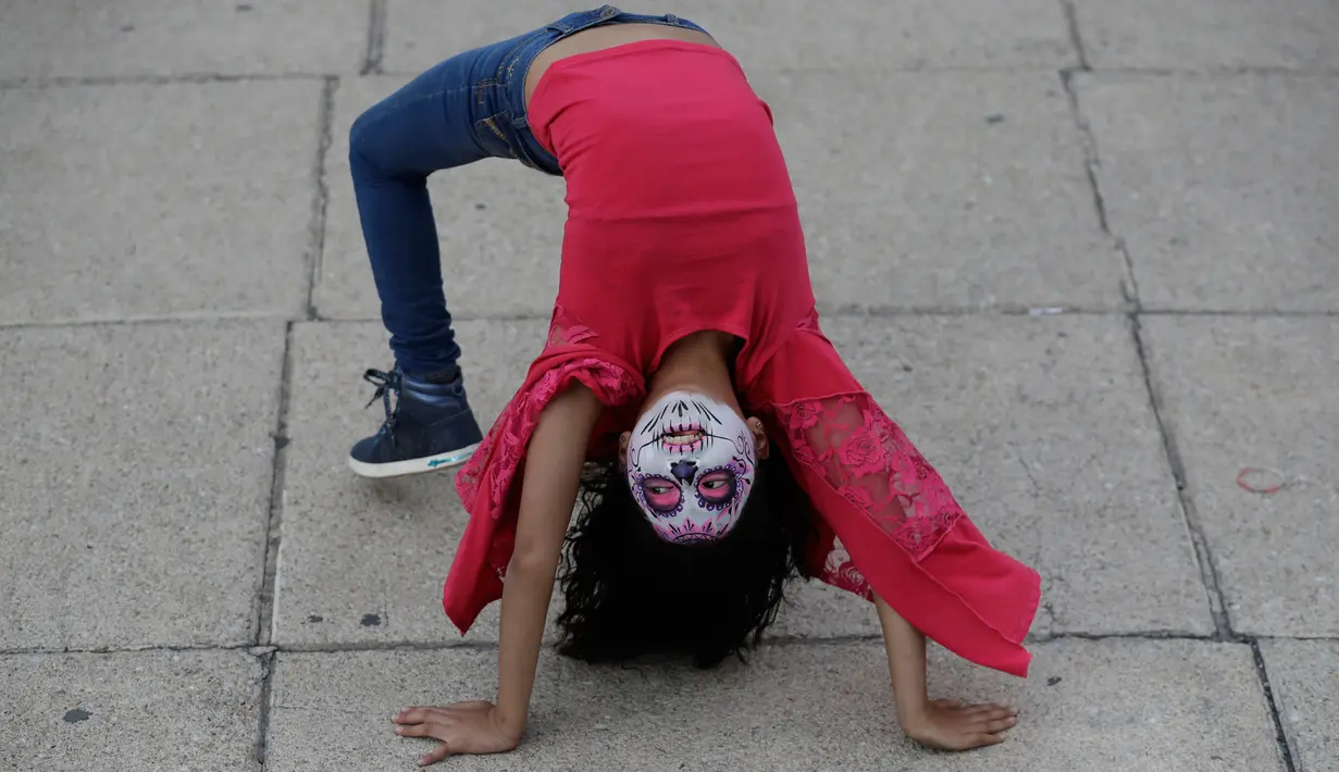 Seorang gadis berdandan sebagai "Catrina" atau wanita kerangka menunggu dimulainya Prosesi Grand Catrinas, bagian dari perayaan Day of The Dead, di Mexico City, Minggu (22/10). Acara ini untuk mengenang mendiang kerabat dan sahabat. (AP/Rebecca Blackwell)