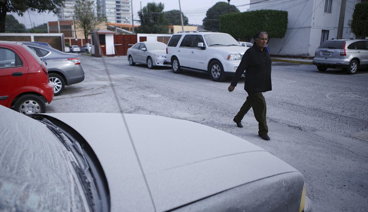Seorang wanita berjalan dibelakang mobil dibelakang mobil ang tertutup abu vulkanik setelah letusan awal gunung berapi Popocatepetl di Puebla, Meksiko, (18/4). (REUTERS/Imelda Medina)