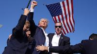 Kandidat presiden dari Partai Republik Donald Trump dikelilingi oleh petugas keamanan, yang menggiringnya turun dari panggung sebuah rapat umum di Buttler, Pennsylvania, Sabtu (13/7/2024) sore waktu setempat. (AP Photo/Evan Vucci)
