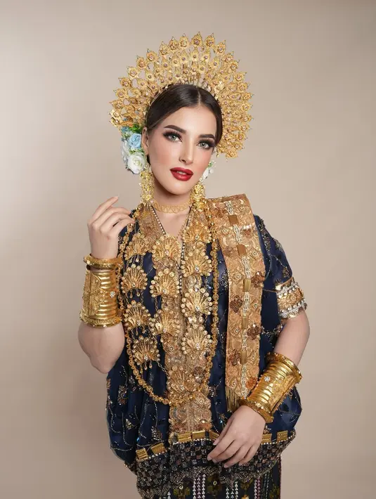 Busana Minang yang ia kenakan kian menyempurnakan keseluruhan look. Mahkota suntiang emas megah berdiri anggun di kepalanya, dipadu dengan suntiang bunga melati di sisi kanan-kiri yang menambah kesan feminin. Aksesoris emas berlapis, dari kalung panjang, anting besar, gelang, hingga pending, menjadi simbol kemakmuran sekaligus keanggunan adat Minang.
