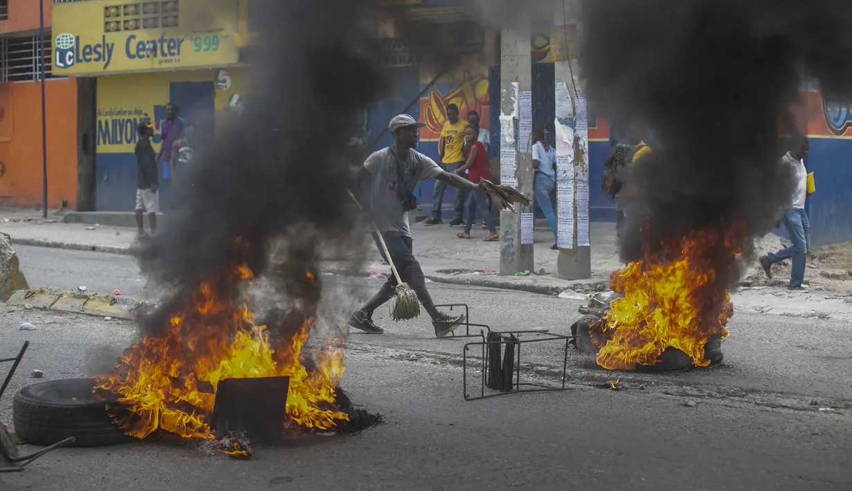 Seorang pria menambahkan puing-puing untuk dibakar di barikade ban yang terbakar yang dipasang oleh pengunjuk rasa selama demonstrasi menuntut Perdana Menteri Haiti Ariel Henry mundur dan menyerukan kualitas hidup yang lebih baik, di Port-au-Prince, Haiti, Senin (29/8/2022). (AP Photo/Odelyn Joseph)