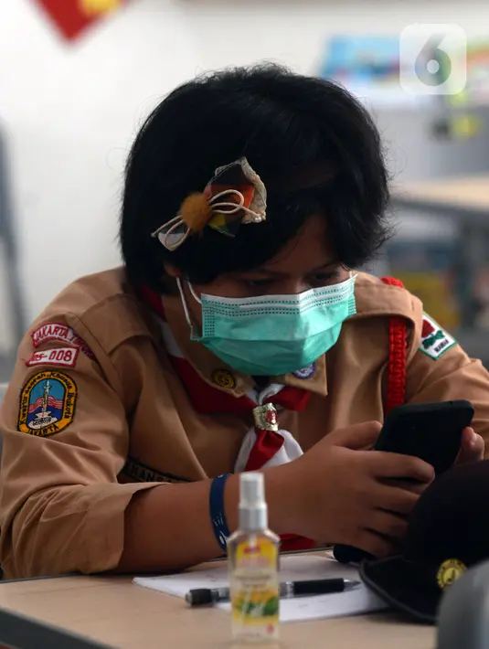 Seorang murid melihat gawai saat uji coba pembelajaran tatap muka di SDN Malaka Jaya 07 Jakarta, Rabu (9/6/2021). Uji coba pembelajaran tatap muka diikuti dengan jumlah siswa terbatas, menerapkan jaga jarak, dan mengenakan masker untuk menghindari penularan COVID-19. (merdeka.com/Imam Buhori)