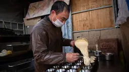 Seorang pedagang menuangkan adonan ke dalam cetakan kue di pasar di Beijing (20/11). (AFP Photo/Nicolas Asfouri)