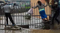 Pejalan kaki berjalan di pagar untuk menyebrang menyusuri jalan yang banjir menuju tempat kerja setelah hujan deras di Nairobi, Kenya (15/3). (AFP Photo/Simon Maina)
